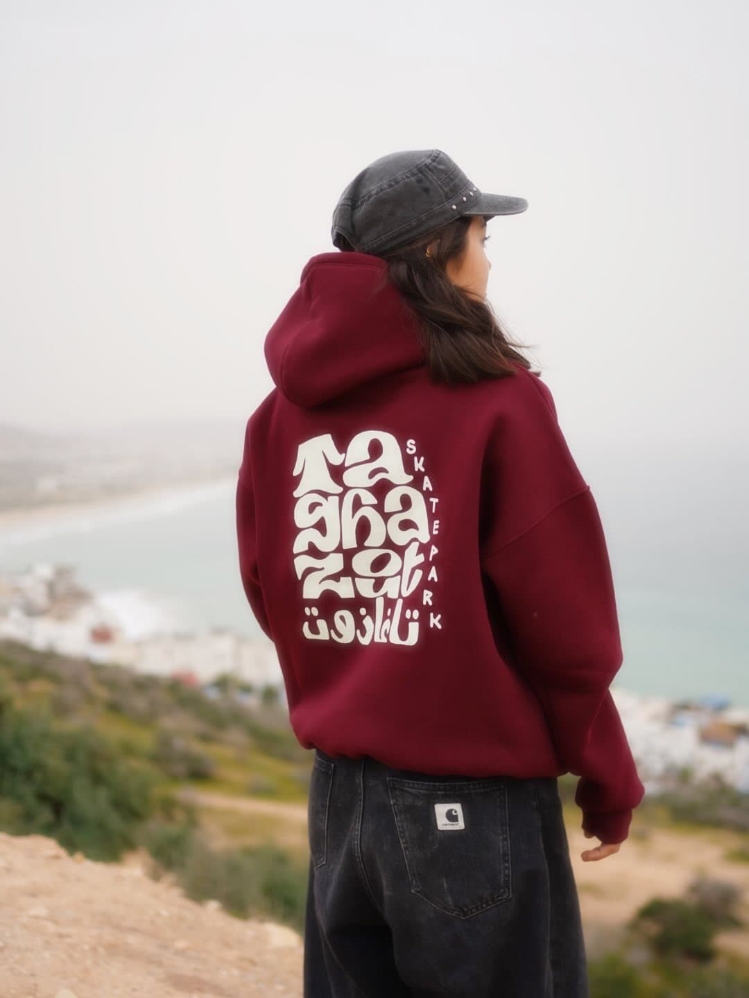 The burgundy Taghazout Skatepark hoodie from behind, its Arabic and Latin back print facing the bay